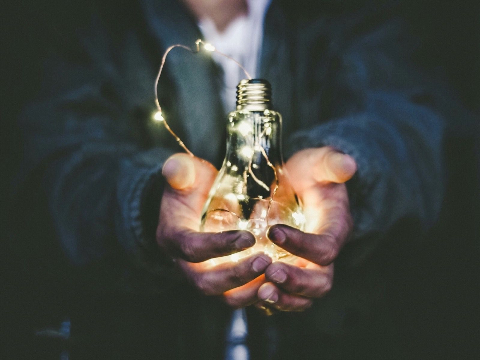 Cupped hands holding a glowing lightbulb wrapped in string lights
